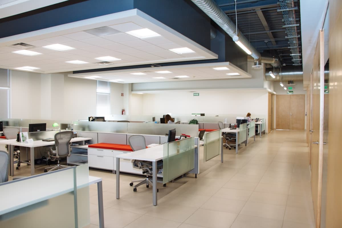 Escritório corporativo moderno, com mesas de trabalho organizadas e divisórias de vidro fosco, representando ambiente de governança e conformidade empresarial