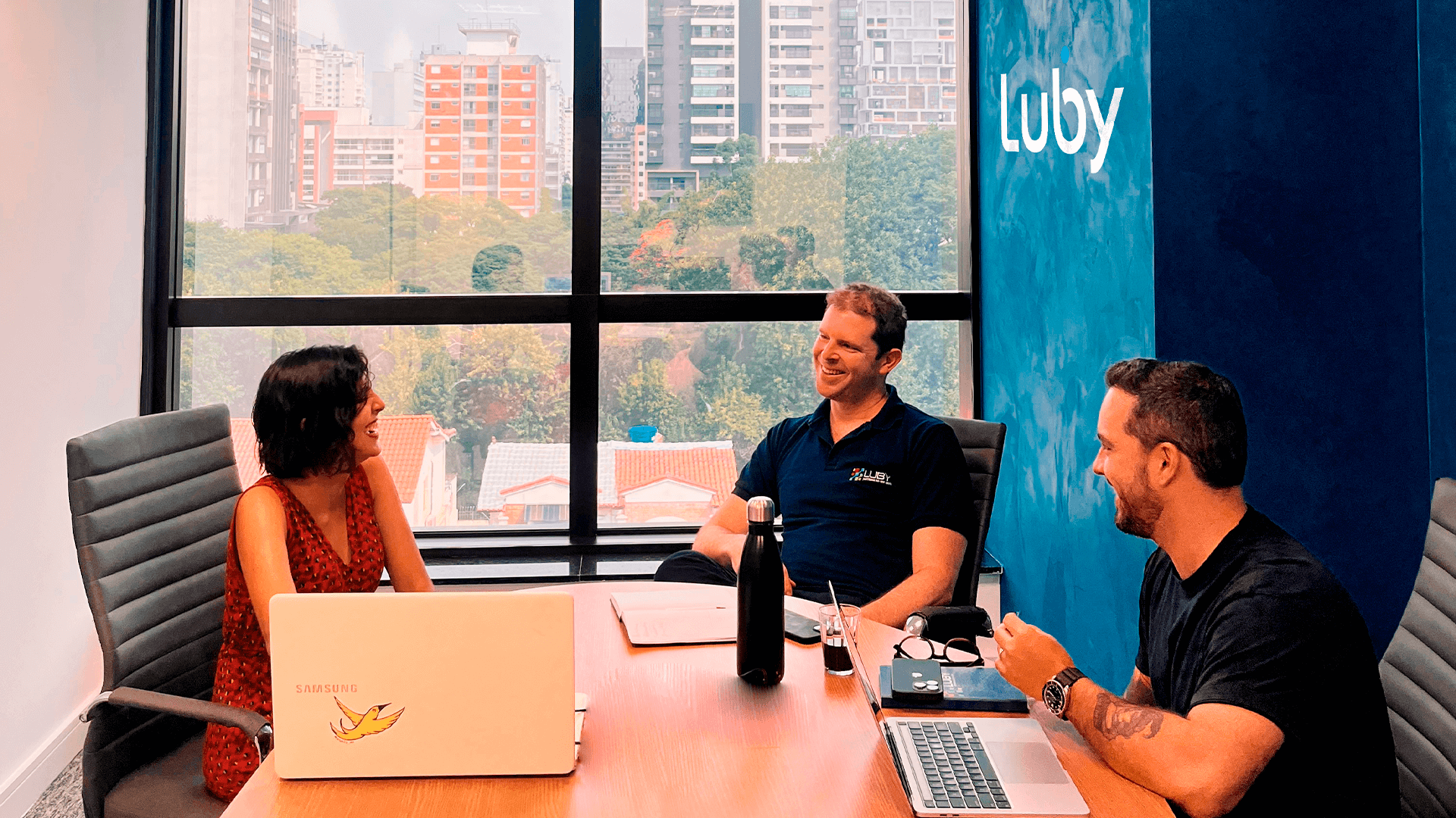 Profissionais da Luby, empresa de tecnologia, reunidos na sede da empresa conversando sobre negócios.