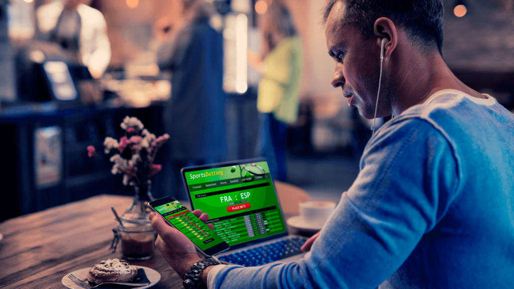 Homem com computador e celular ligado para realizar pagamentos de apostas online.